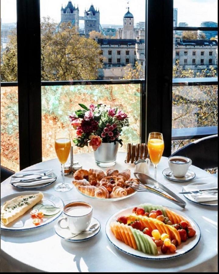 Tower Suites By Blue Orchid لندن المظهر الخارجي الصورة The photo showcases a beautifully set breakfast table with a scenic view through large glass windows. The table features an array of items, including:

1. A small vase filled with colorful flowers.
2. Two glasses of orange juice.
3. A cup of coffee o