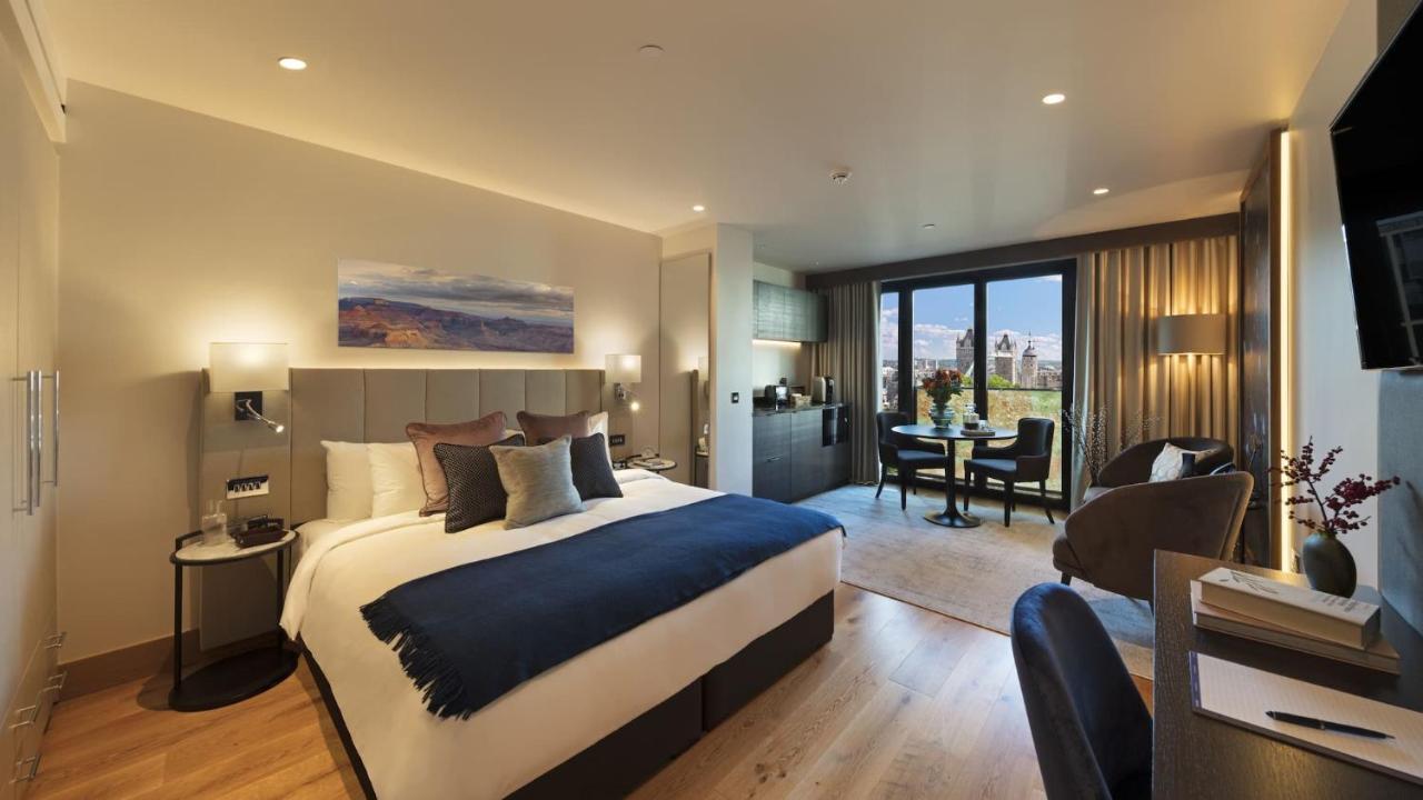 Tower Suites By Blue Orchid لندن المظهر الخارجي الصورة The photo shows a modern hotel room. It features a large bed with a dark blue throw blanket and several decorative pillows. The walls are painted in neutral tones, and there's a landscape painting above the bed. To one side, there is a small kitchene