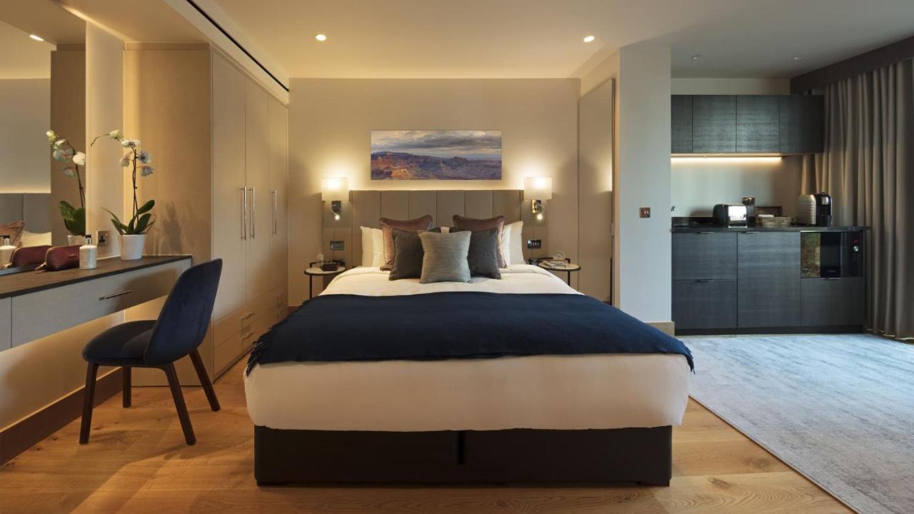 Tower Suites By Blue Orchid لندن المظهر الخارجي الصورة The photo displays a modern hotel room featuring a plush bed with a dark blue bedspread and several decorative pillows. The walls are adorned in neutral tones, and there is a piece of artwork above the bed depicting a serene landscape. On the side, t