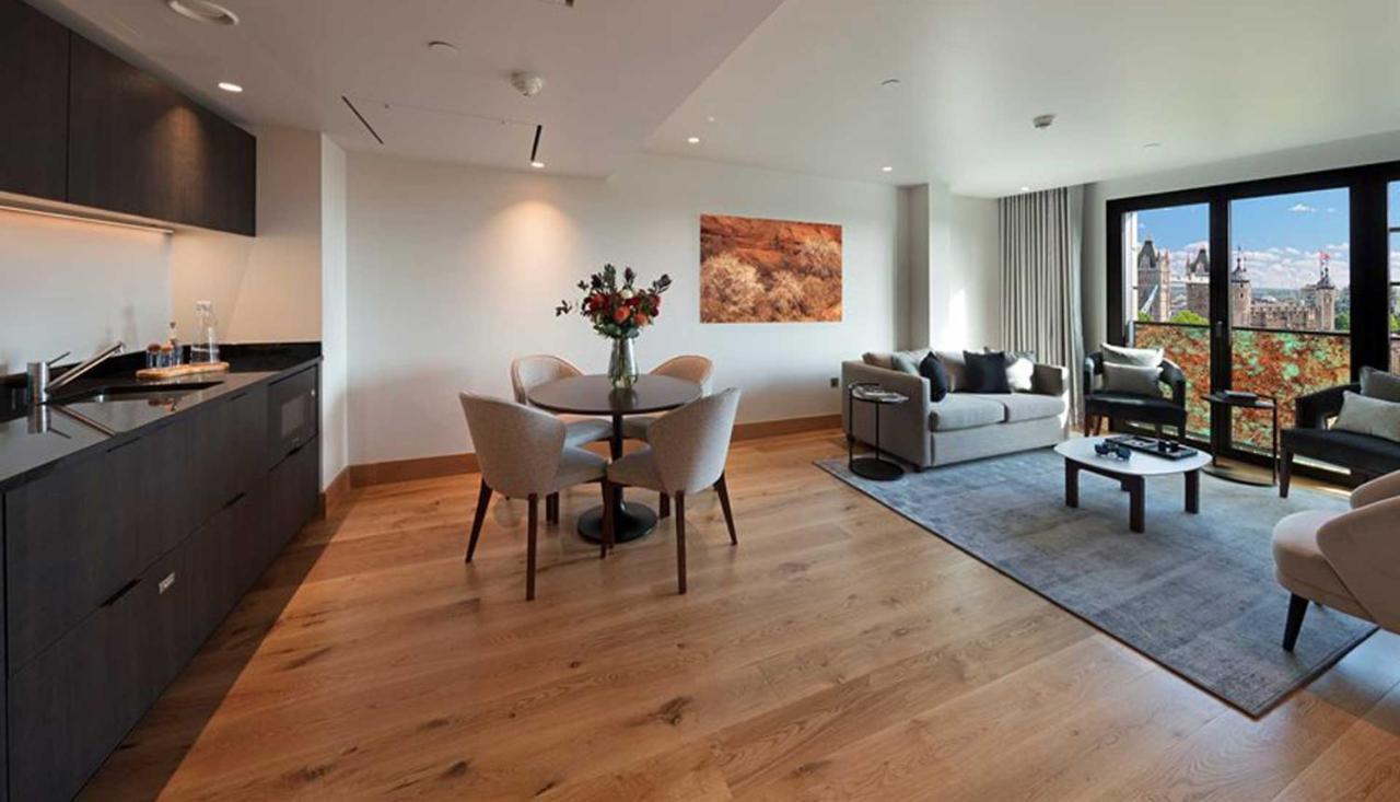 Tower Suites By Blue Orchid لندن المظهر الخارجي الصورة The photo shows a modern apartment interior. On the left side, there is a kitchen area with dark cabinetry, while on the right side, a comfortable living area is visible. In the center, a round dining table is set with four chairs and a vase of flowe