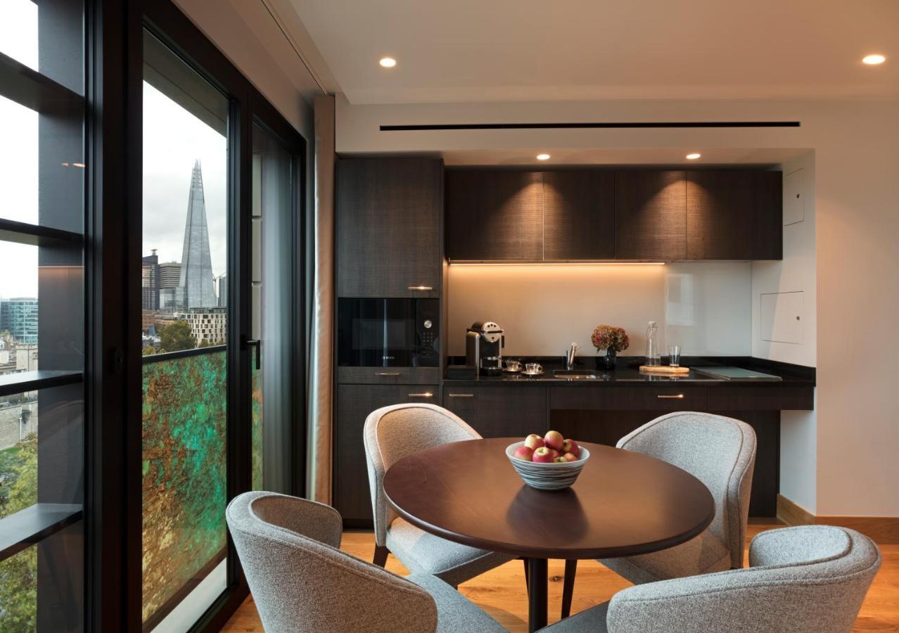 Tower Suites By Blue Orchid لندن المظهر الخارجي الصورة The photo shows a modern kitchen and dining area. It features a round table with four gray chairs, and a bowl of apples is placed in the center of the table. The kitchen has dark cabinetry, a black countertop, and built-in appliances. Large windows a