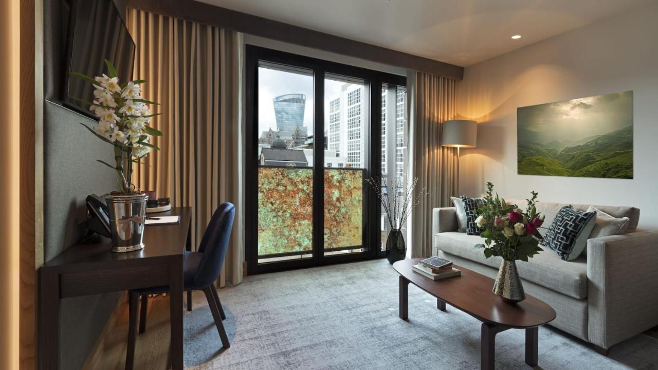 Tower Suites By Blue Orchid لندن المظهر الخارجي الصورة The photo shows a modern and well-lit living space. There is a comfortable sofa with decorative cushions, a small coffee table in front of it, and a floor lamp providing additional lighting. Beside the sofa, there are decorative plants and a vase wit