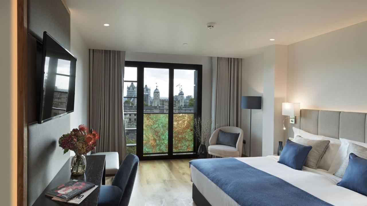 Tower Suites By Blue Orchid لندن المظهر الخارجي الصورة The photo shows a modern hotel room featuring a large bed with blue and white bedding, a cozy armchair, and a small desk. There is a flat-screen television mounted on the wall across from the bed. The room has large glass doors leading to a balcony o