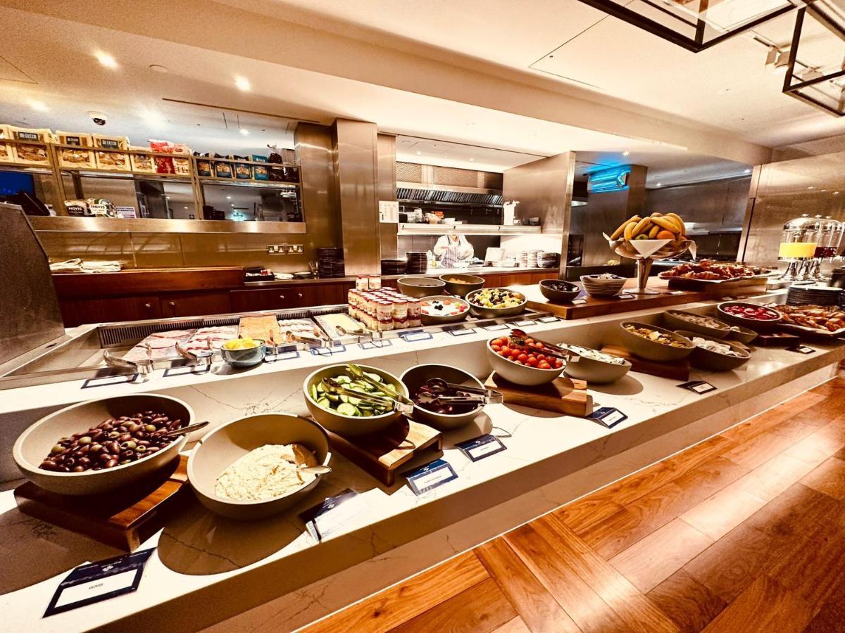 Tower Suites By Blue Orchid لندن المظهر الخارجي الصورة The photo shows a well-organized buffet spread. There are several bowls filled with various ingredients, likely for a meal or a salad bar. The ingredients include different types of vegetables, fruits, and possibly some grains or legumes. In the back