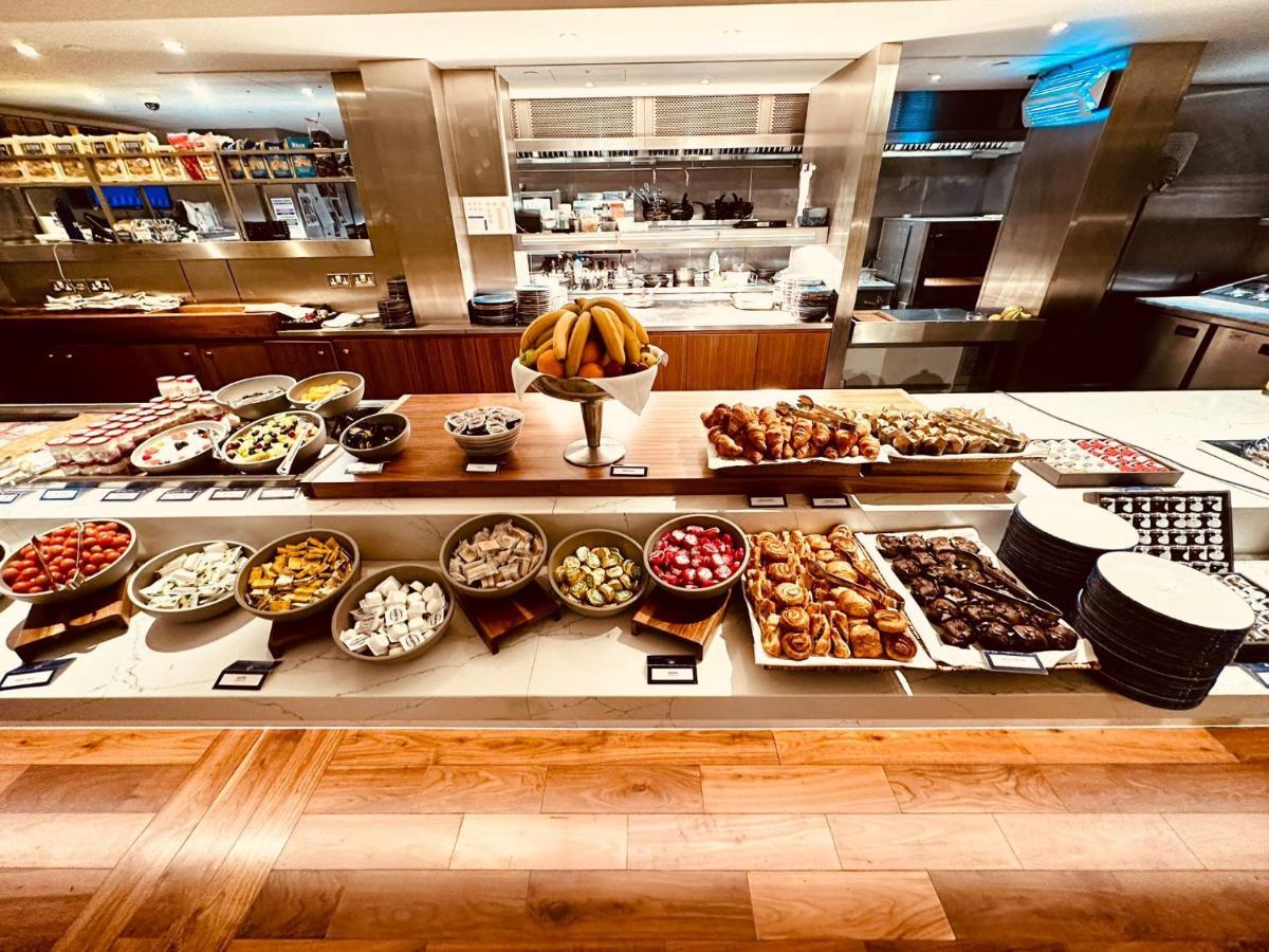 Tower Suites By Blue Orchid لندن المظهر الخارجي الصورة The photo displays a beautifully arranged buffet featuring a variety of food items. There are several bowls and platters filled with colorful fruits, pastries, and desserts. In the center, a large bowl of bananas is prominently placed. Surrounding th